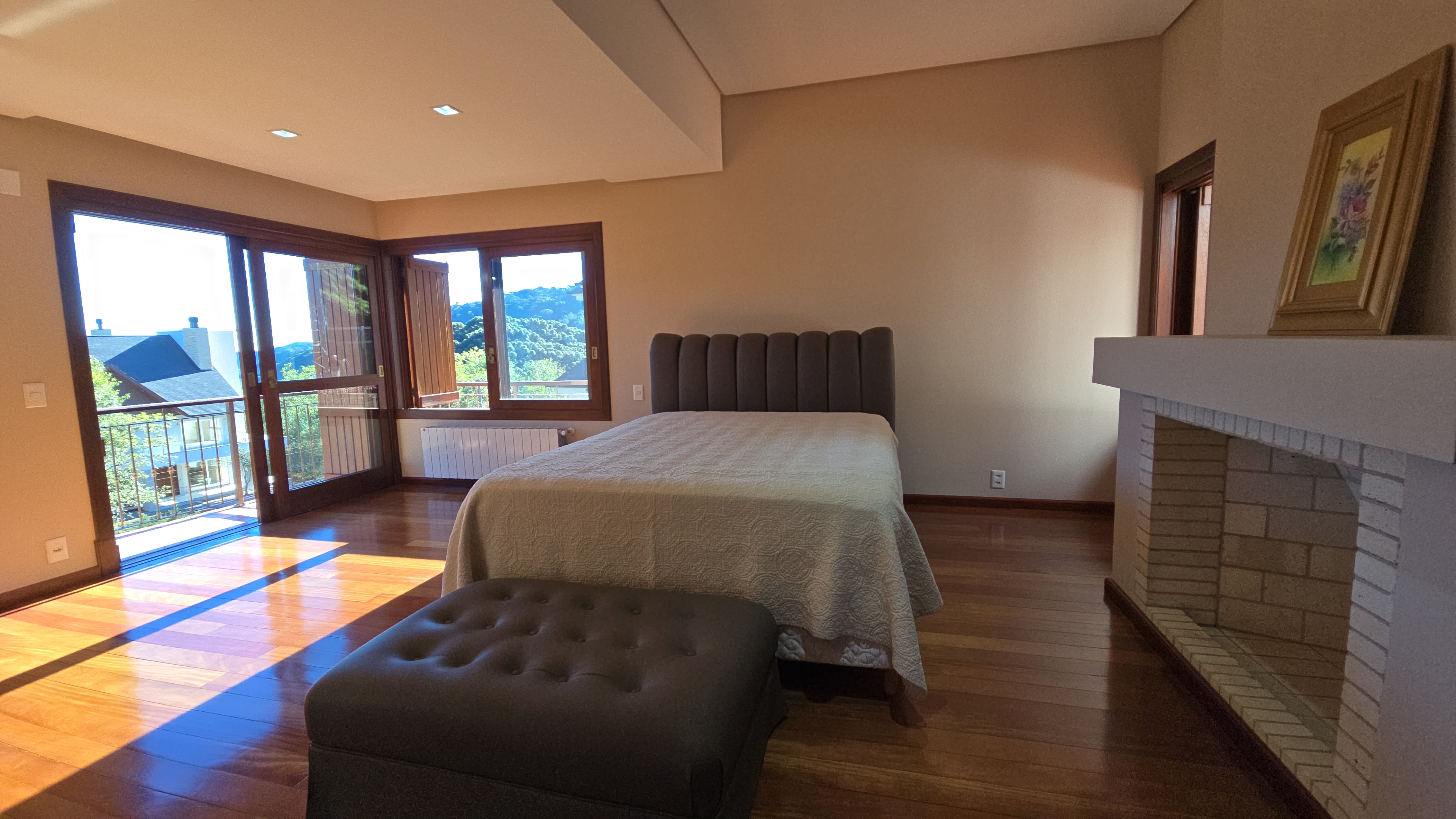 Suíte master da Mansão La Guapa com sacada, vista para a serra, lareira e piso de madeira